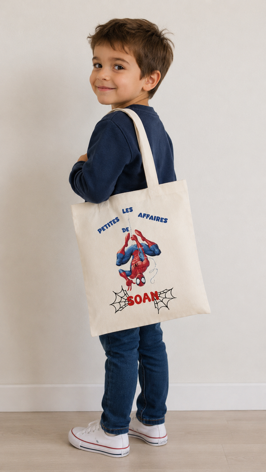 Tote bag enfant personnalisé avec prénom et illustration Spiderman, sac en coton naturel porté à l'épaule par un jeune garçon.