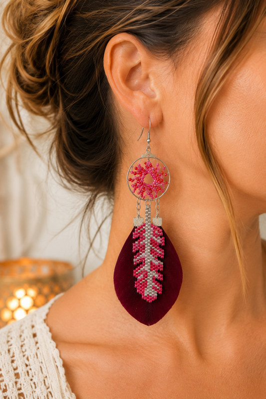 Gros plan sur une boucle d’oreille attrape-rêves avec tissage de perles Miyuki roses, rouges et argentées et plume bordeaux.