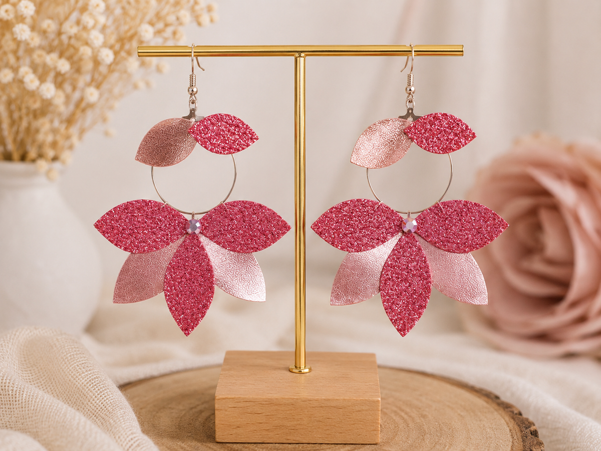 Paire de boucles d’oreilles lotus inversé rose pailleté présentée sur un support à bijoux.