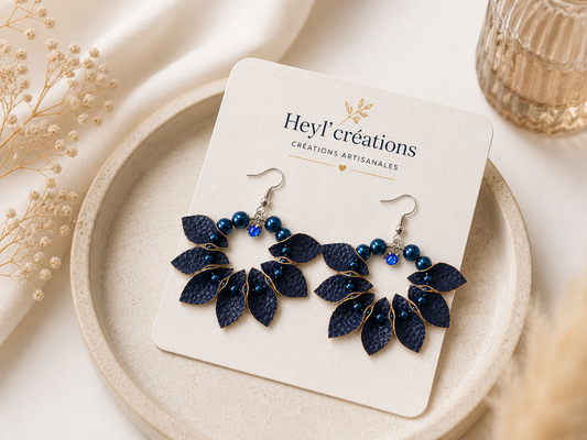 Boucles d’oreilles en simili cuir bleu avec perles posées sur carte de marque Heyl’créations