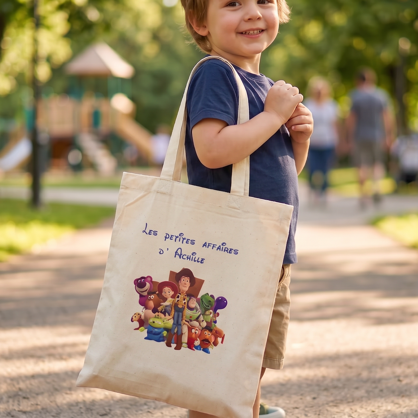 Tote bag enfant personnalisé avec prénom, sac en coton écru porté à l’épaule par un jeune enfant et illustré d’un univers de jouets colorés.